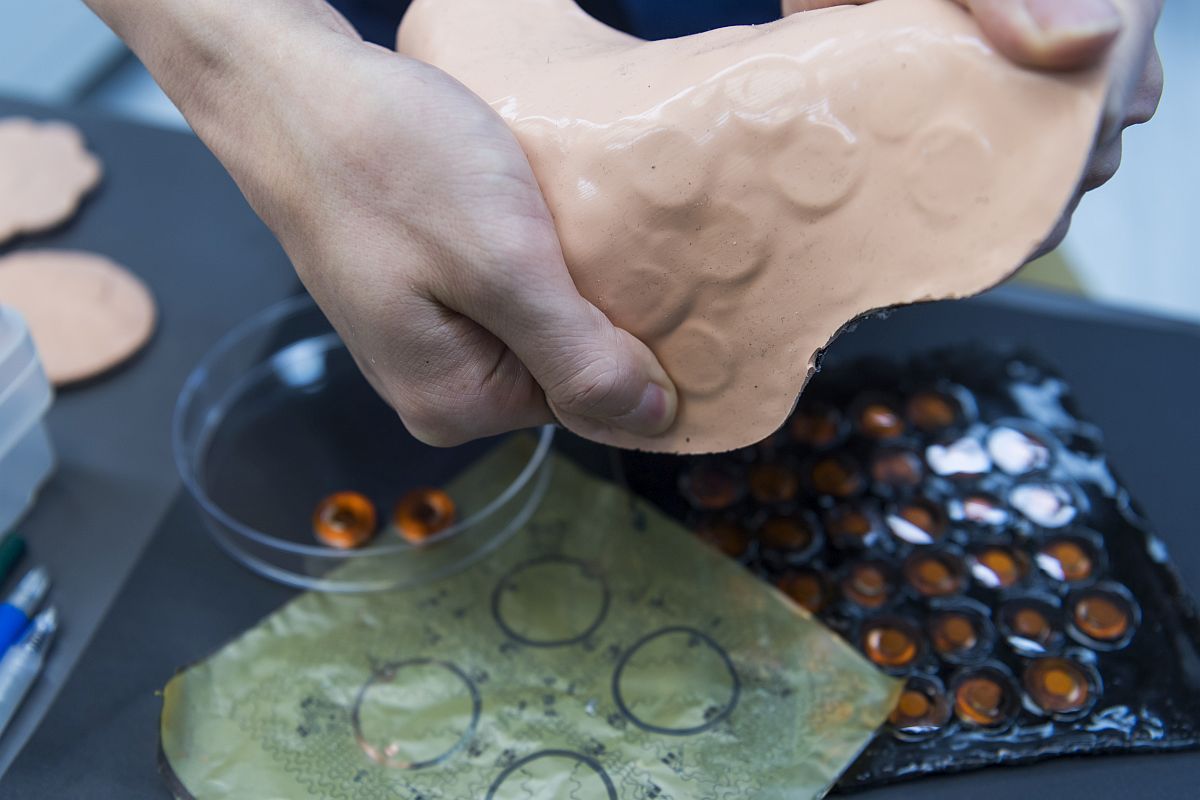 皮膚VR裝置的厚度僅為3 毫米，可彎曲的彈性薄層裡藏着數百個功能組件。圖中一個個的橙色圓塊就是致動器，通過裝置中8個獨立可控制的通信埠，分4組控制共32個致動器。